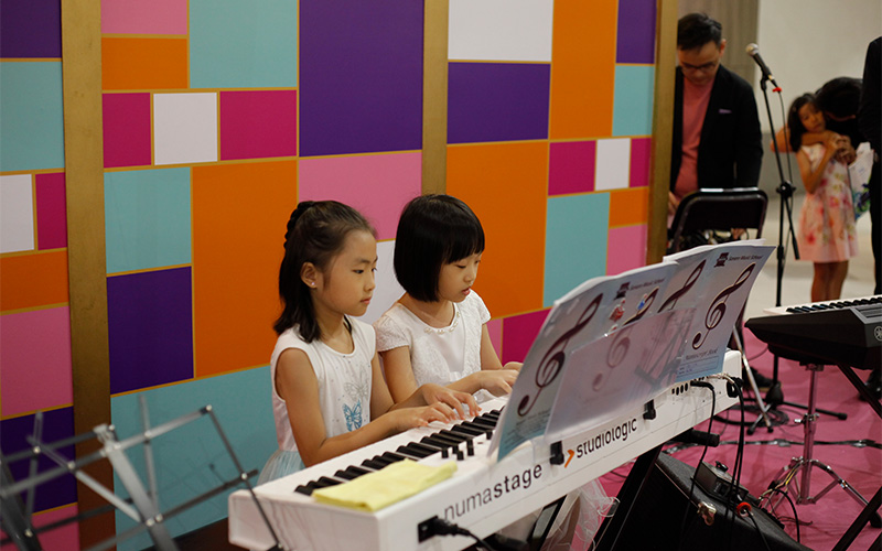 Two young girls reading notes while playing the piano together.