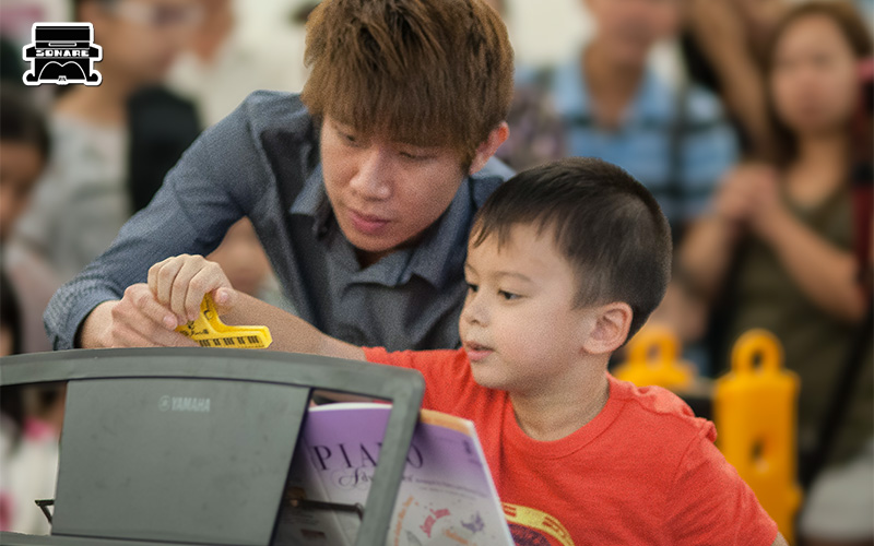 Music instructor guiding young child at a piano keyboard lesson.