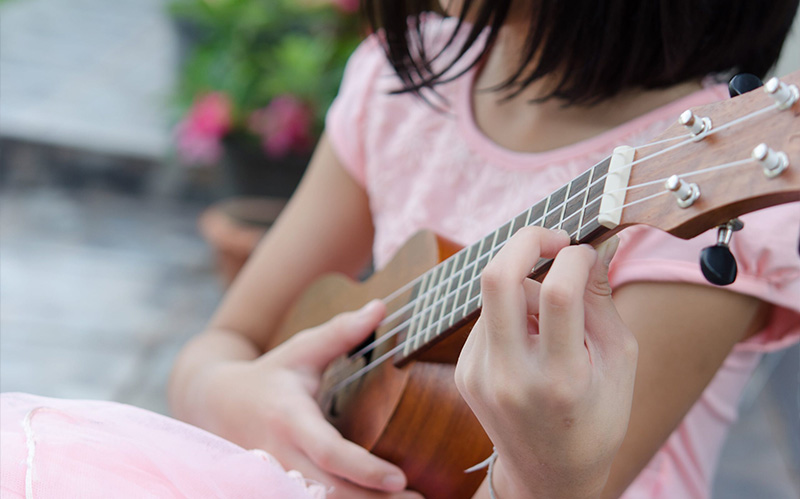 Close-up of a child playing a wooden ukulele.