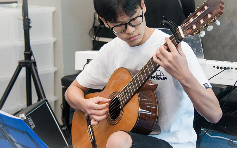 Teenage boy playing an acoustic guitar during a music performance.