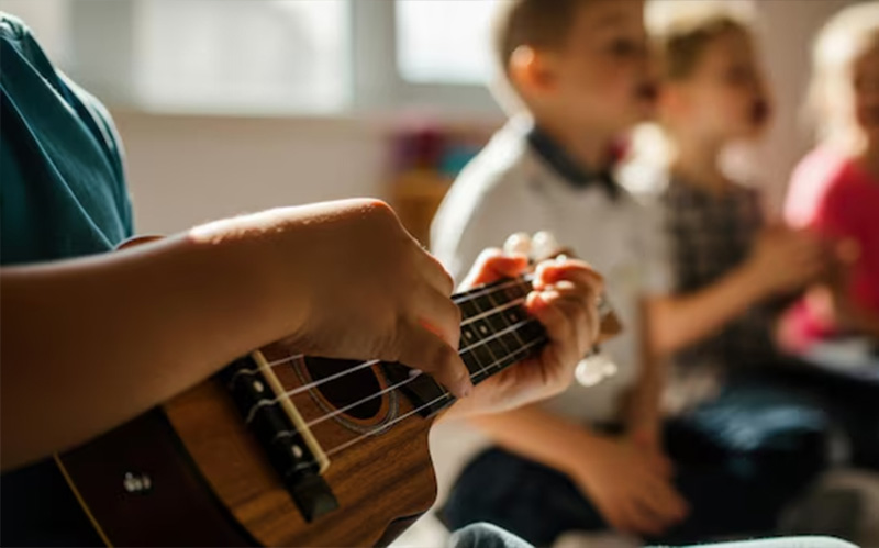 Children playing ukuleles together in a music classroom.