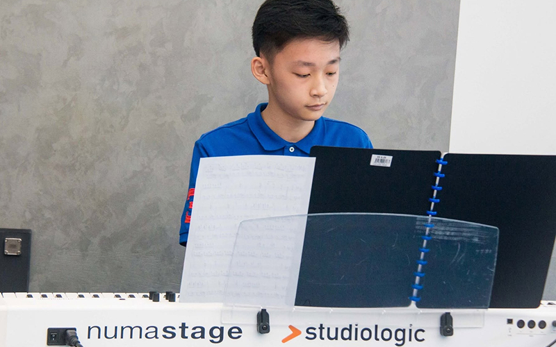 Teenage boy playing a digital piano at a music event.