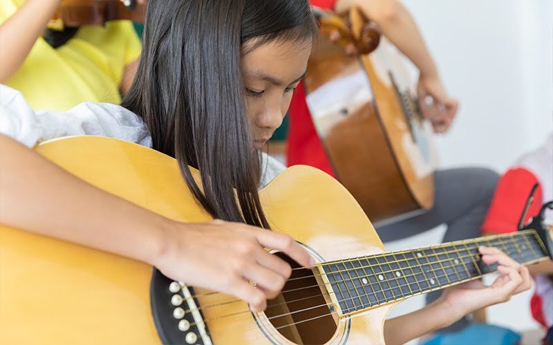 Young girl focused on playing acoustic guitar.