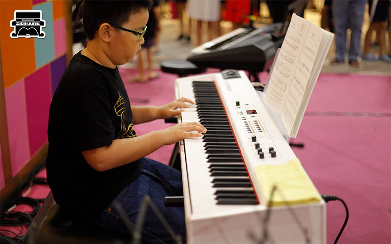 Young student practicing keyboard at a Sonare Music school event.