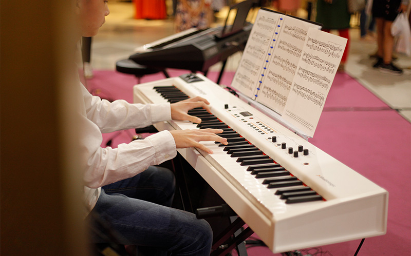 Student playing a white digital piano with sheet music.
