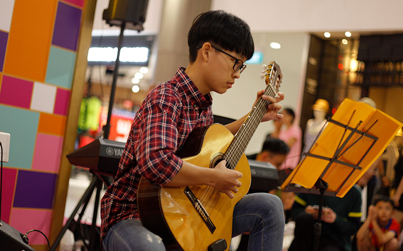 Young boy playing classical guitar looking at music stand.